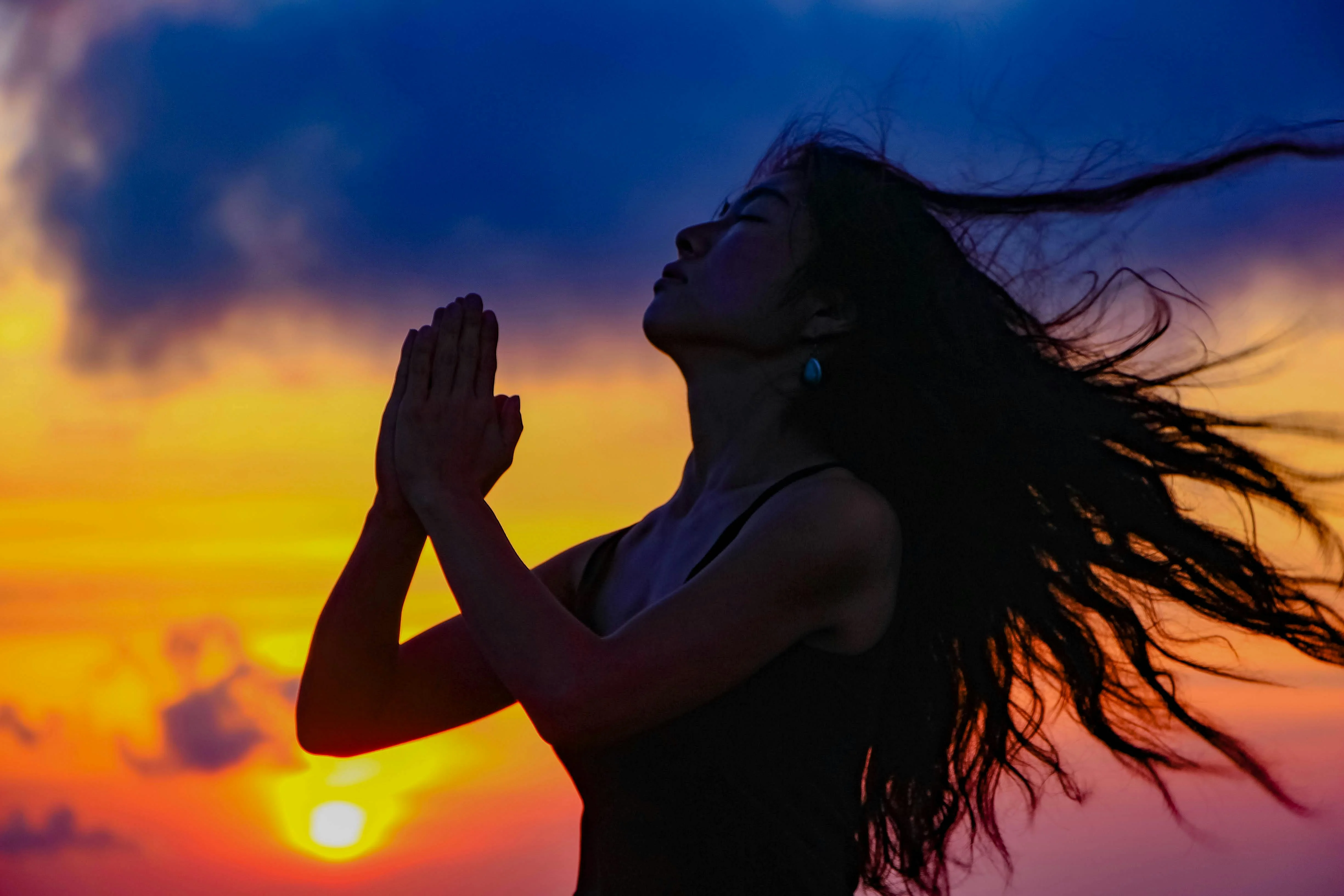 A woman with her hands in prayer and her hair blowing, silhouetted against a sunset, shown as a TikTok live stream