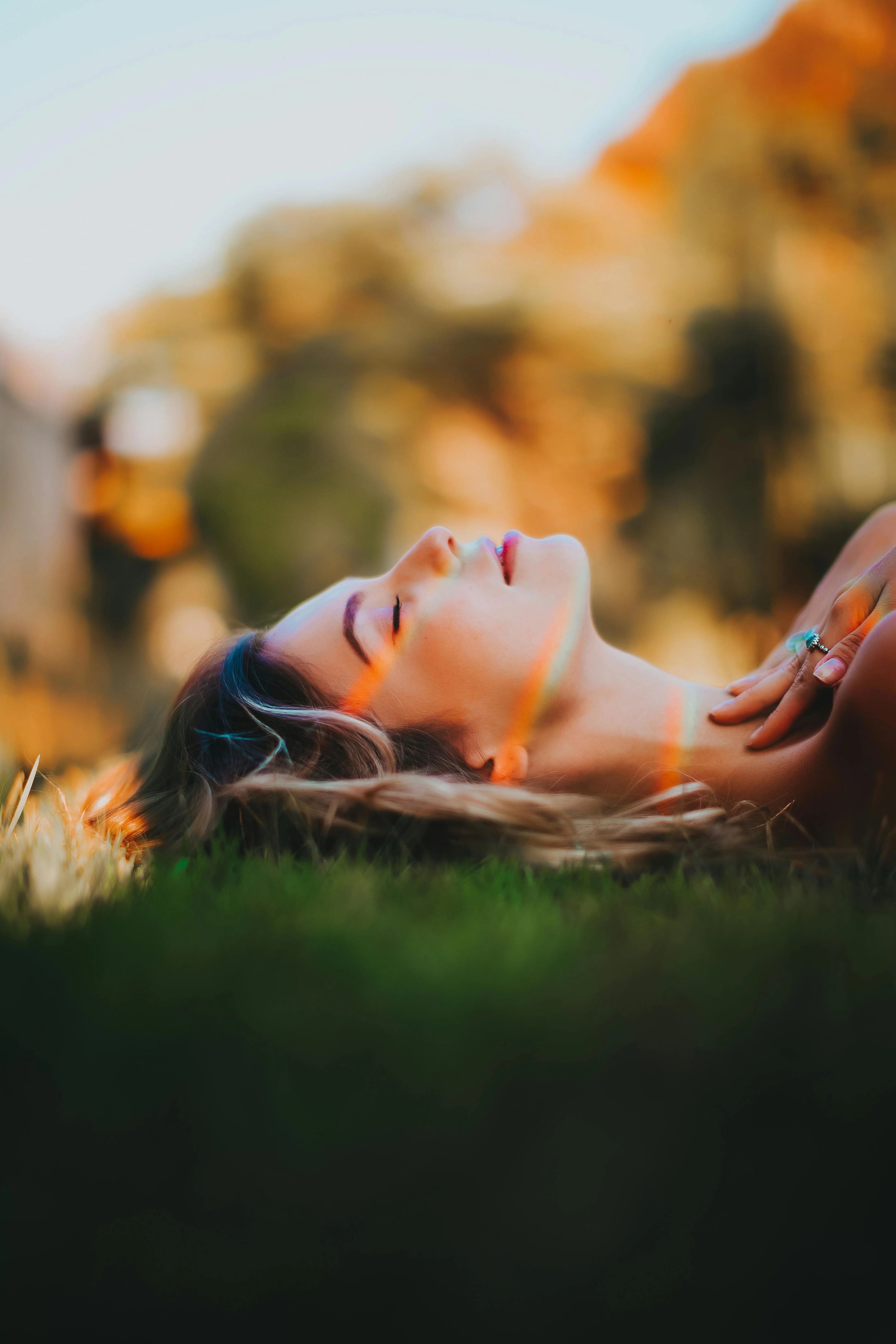 A woman lies in the grass with her eyes closed, light falling across her face