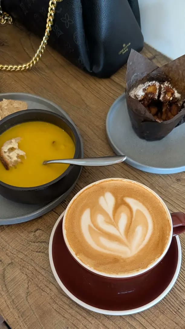 Soup, a latte and a muffin on a wooden cafe table