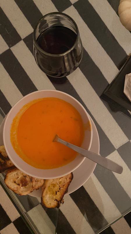 A bowl of orange soup beside toast and a glass of red wine