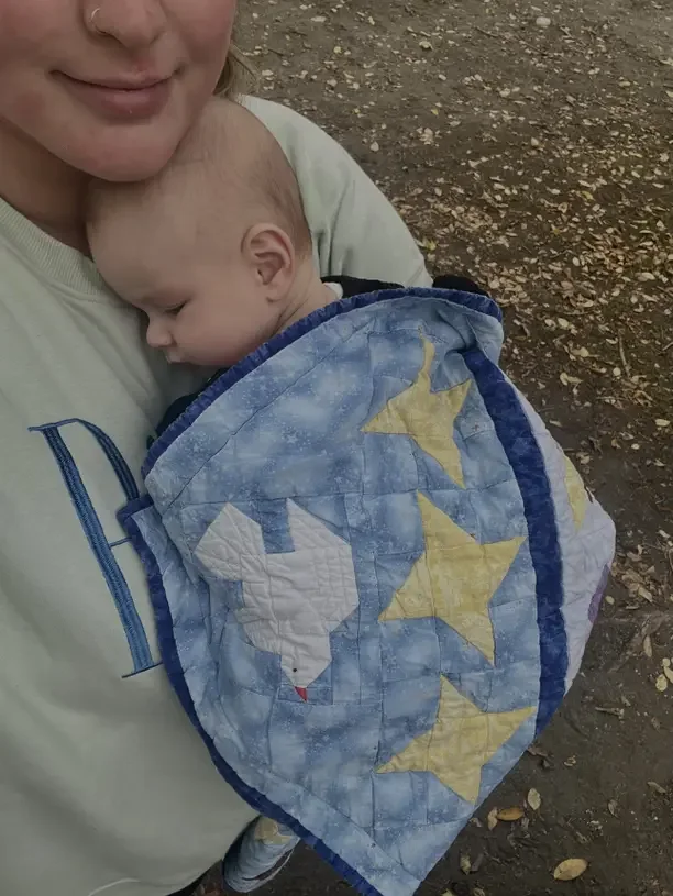 A mother cuddles her sleeping baby wrapped in a blue blanket covered in stars