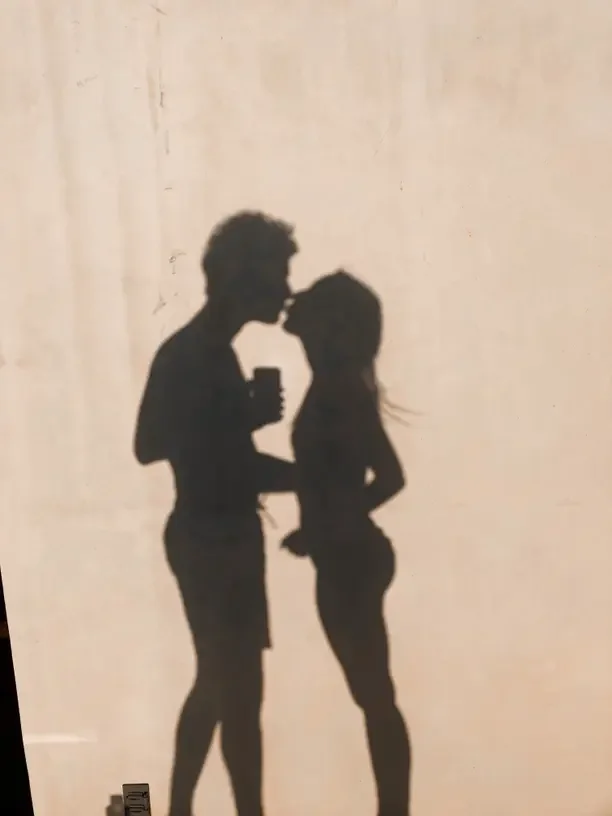 Shadows of a couple leaning in for a kiss on a pale plaster wall